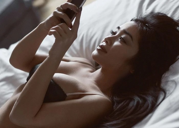 asian woman lying in bed with phone