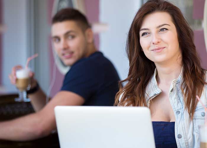 man with glass of coffee lokin at woman with laptop